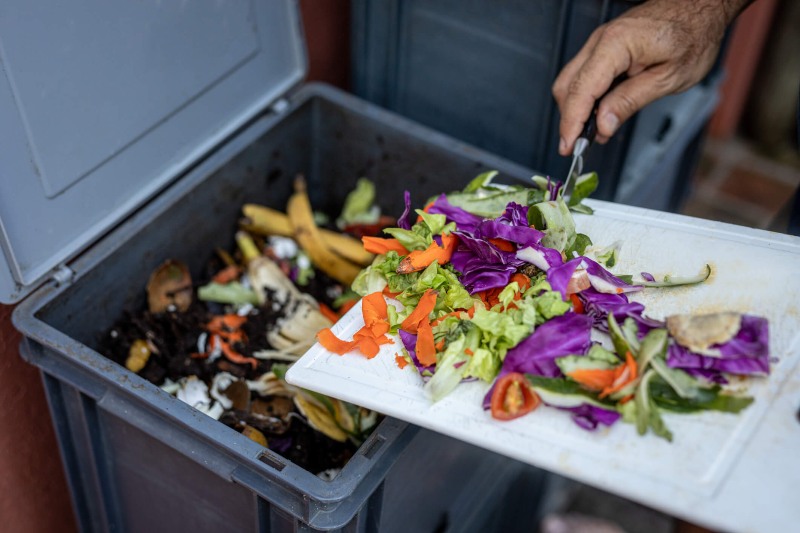 Person adding vegetable scraps to a compost bin for organic waste recycling in Franklin, TN
